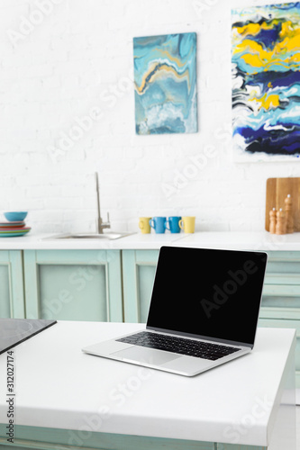 selective focus of laptop with kitchenware and abstract paintings on background