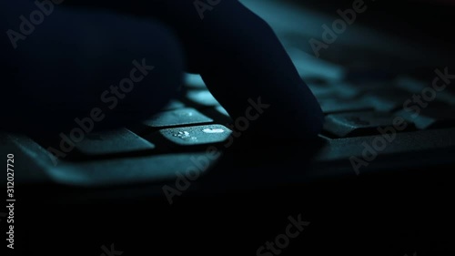 Close up of typing on laptop keyboard in the darkness.