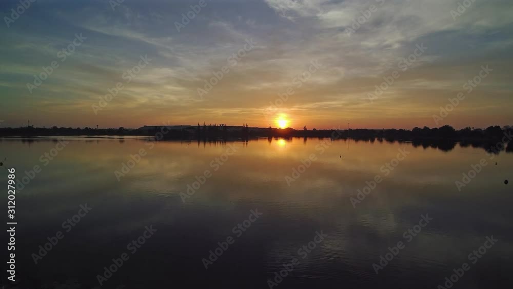 Vdo. Aerial view evening above the lake, view of yellow sun light with reflection on surface of water and cloudy sky background, sunset at Krajub reservoir, Ban Pong District, Ratchaburi, Thailand. Vdo. Aerial view evening above the lake, view of yellow sun light with reflection on surface of water and cloudy sky background, sunset at Krajub reservoir, Ban Pong District, Ratchaburi, Thailand.