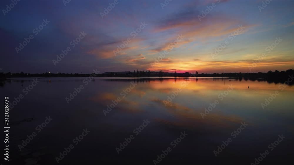 Vdo. Aerial view evening above the lake, view of red sun light with reflection on surface of water and cloudy sky background, twilight at Krajub reservoir, Ban Pong District, Ratchaburi, Thailand. Vdo. Aerial view evening above the lake, view of red sun light with reflection on surface of water and cloudy sky background, twilight at Krajub reservoir, Ban Pong District, Ratchaburi, Thailand.
