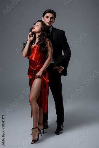 Romantic couple in suit and red silk dress hugging on grey