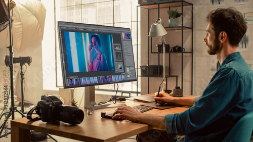 Professional Photographer Sitting at His Desk Uses Desktop Computer in a Photo Studio Retouches. After Photoshoot He Retouches Photographs of Beautiful Female Model in an Image Editing Software