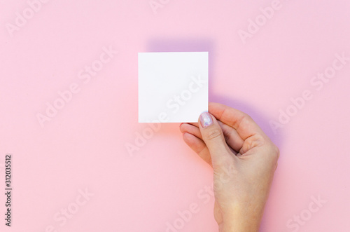 Small love letter mockup Valentine with your message. White card on a pink background. Female hand holds card top view mockup