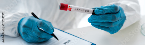 panoramic shot of scientist writing and holding test tube with lettering dna test