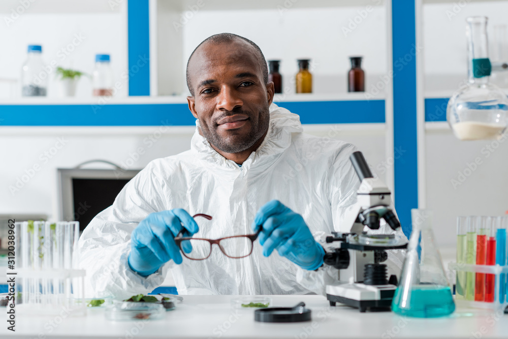 smiling african american biologist holding glasses and looking at camera smiling african american biologist holding glasses and looking at camera