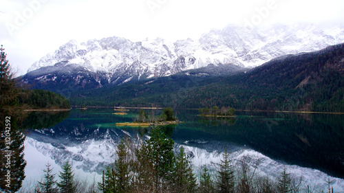 Zugspitze (mountain) in the Alps. Tourism spot. Nice hiking trail around the lake. Fir trees, rock fragments, stones. Zugspitze in background. Insta spot. Reflections in water. Ski region.