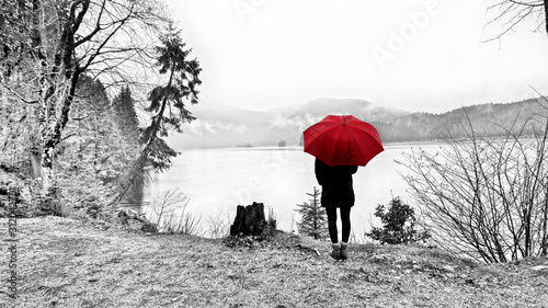 Walk around the Eibsea (Eibsee) near Zugspitze (highest mountain in Germany). Rainy weather. Sea surrounded with fir trees, stones and rock fragments. Wanderer with red umbrella. Black and white.