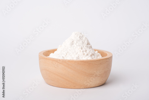 Wheat flour in a brown wooden cup on a white background