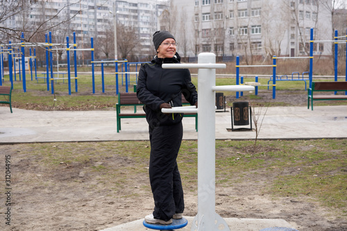 A woman in the early morning is engaged in street simulators. Disc for rotating the waist. Sports, lifestyle