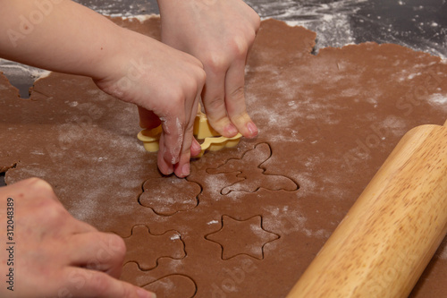 Cutting figures from the dough using special stencils for making ginger Christmas cookies. Children'sand female hands close-up. Home, family prepare for the holidays concept
