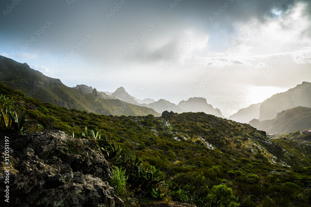 Spain, Tenerife, Dark rain storm clouds on stormy day with sun over mountains of masca canyon at the ocean coast, view above green nature landscape