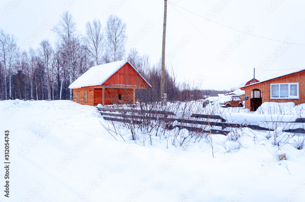 village in winter in the snow on a sunny day. street of wooden houses road at houses near the forest, no people.