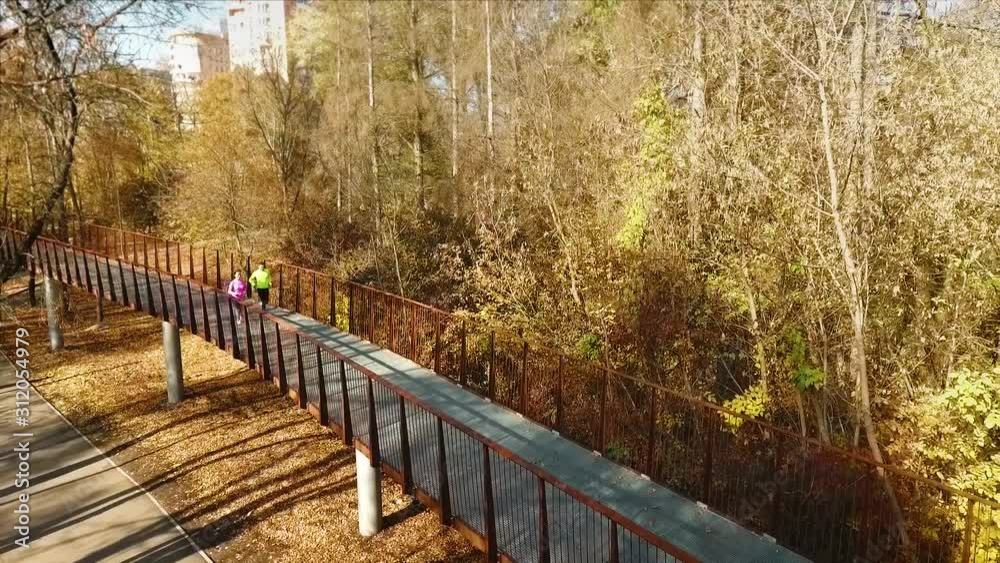 Happy fit couple jogging along metal bridge in autumn park Happy fit couple jogging along metal bridge in autumn park