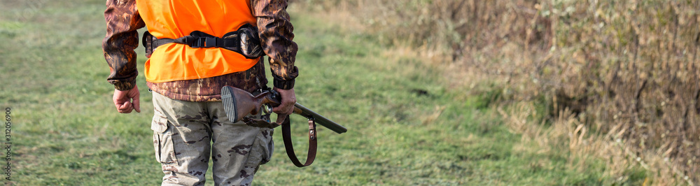 A man with a gun in his hands and an orange vest on a pheasant hunt in a wooded area in cloudy weather. Hunter with dogs in search of game. A man with a gun in his hands and an orange vest on a pheasant hunt in a wooded area in cloudy weather. Hunter with dogs in search of game.