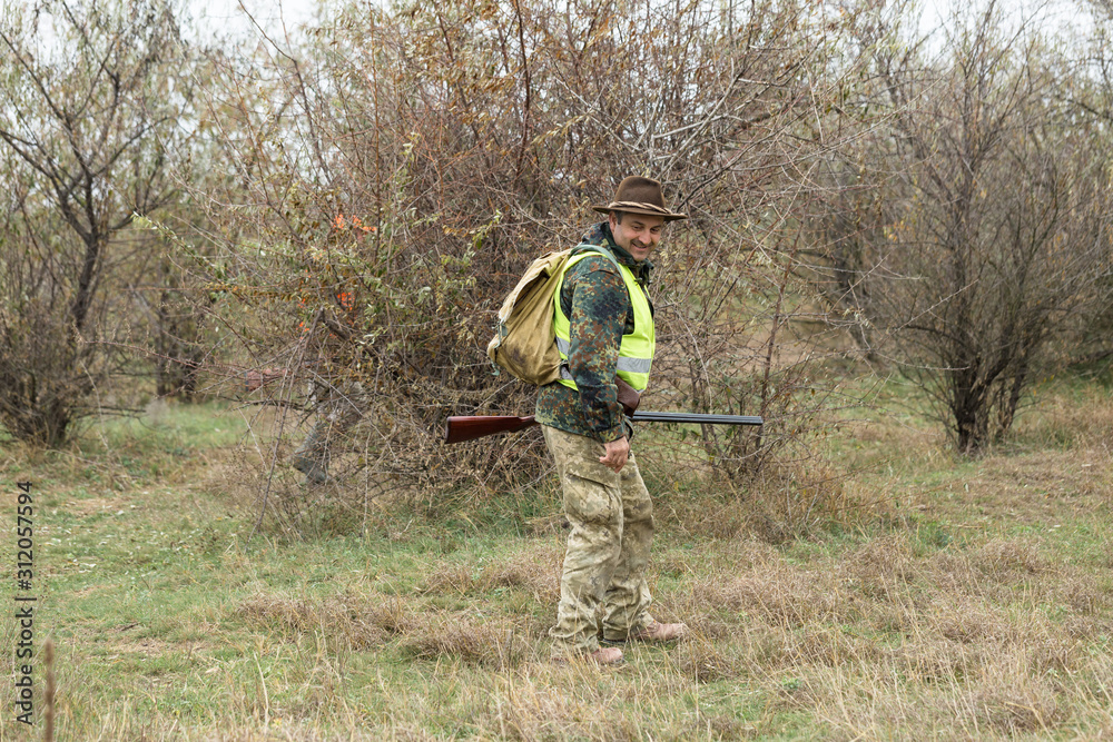 Hunting period, autumn season open. A hunter with a gun in his hands in hunting clothes in the autumn forest in search of a trophy. A man stands with weapons and hunting dogs tracking down the game. Hunting period, autumn season open. A hunter with a gun in his hands in hunting clothes in the autumn forest in search of a trophy. A man stands with weapons and hunting dogs tracking down the game.