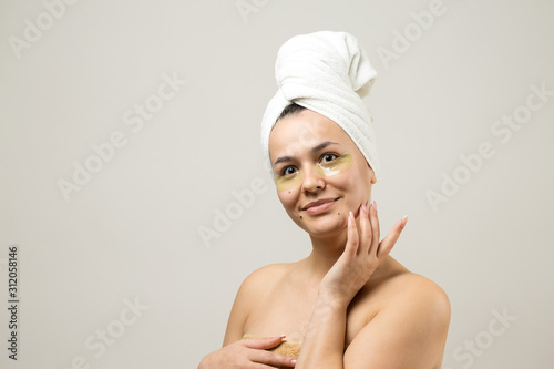 Young beautiful girl in a white towel on his head wears collagen gel patches under her eyes. Mask under eyes treatment face.