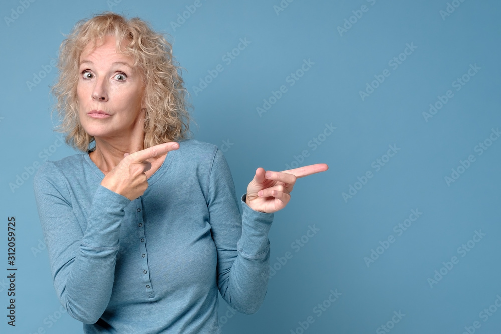 Mature blonde cheerful woman looking aside pointing. Pay attention to this information. Studio shot Mature blonde cheerful woman looking aside pointing. Pay attention to this information. Studio shot