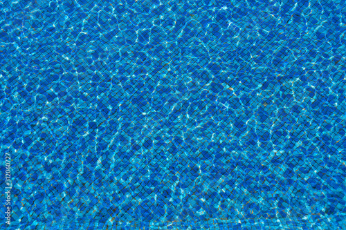 Surface of the pool, waves. The structure of blue tiles through the water.