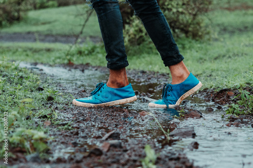 Low angle shot of the leg of person wearing blue shoes in the river stream in forest