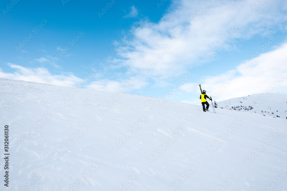 skier in helmet walking with ski sticks on slope in wintertime