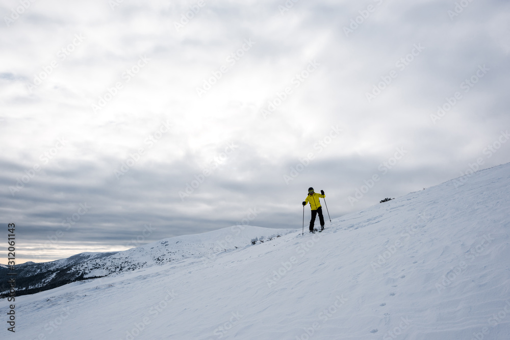 skier in helmet standing with ski sticks on slope in cold wintertime