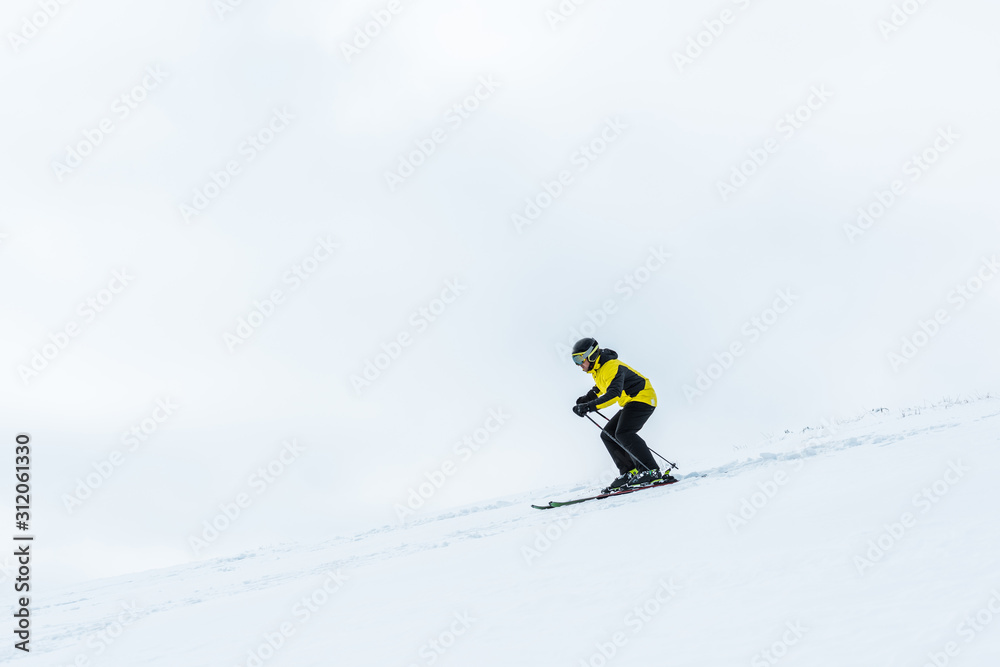 sportsman in helmet holding ski sticks while skiing in wintertime