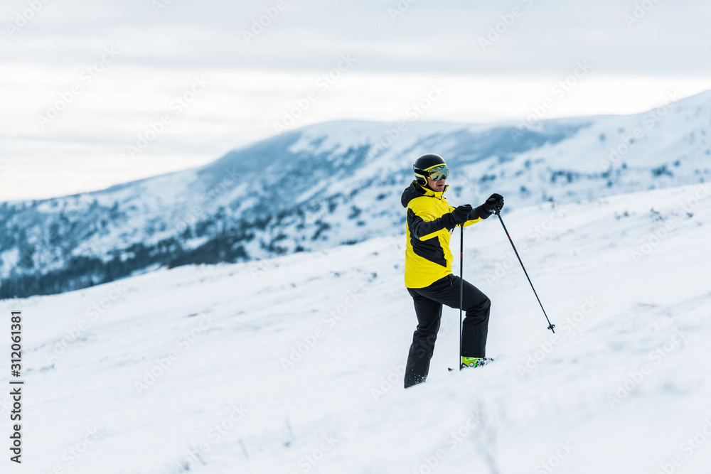 skier in helmet holding sticks and standing on slope in wintertime