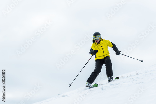 skier in helmet holding sticks and skiing on slope in wintertime