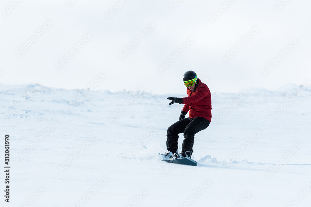 athletic snowboarder in helmet riding on slope outside