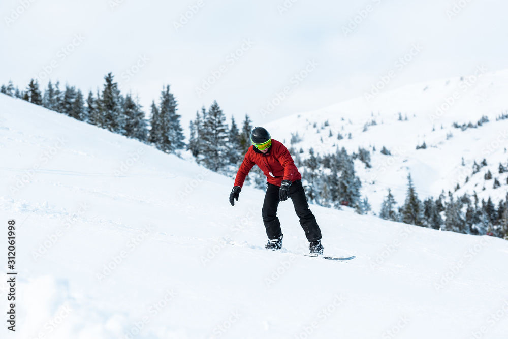 athletic snowboarder in helmet riding on slope in mountains