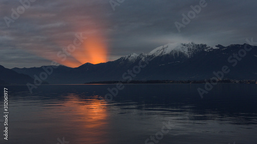 Tramonto sul lago con sole che tramonta e crea cono di luce emergente dalla montagna