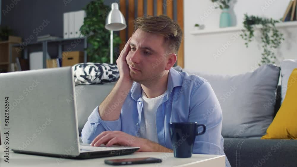 Young man using laptop for work or watching video or use social media. Boy seat on couch in modern living room. Relaxing at home. Slow motion. Young man using laptop for work or watching video or use social media. Boy seat on couch in modern living room. Relaxing at home. Slow motion.