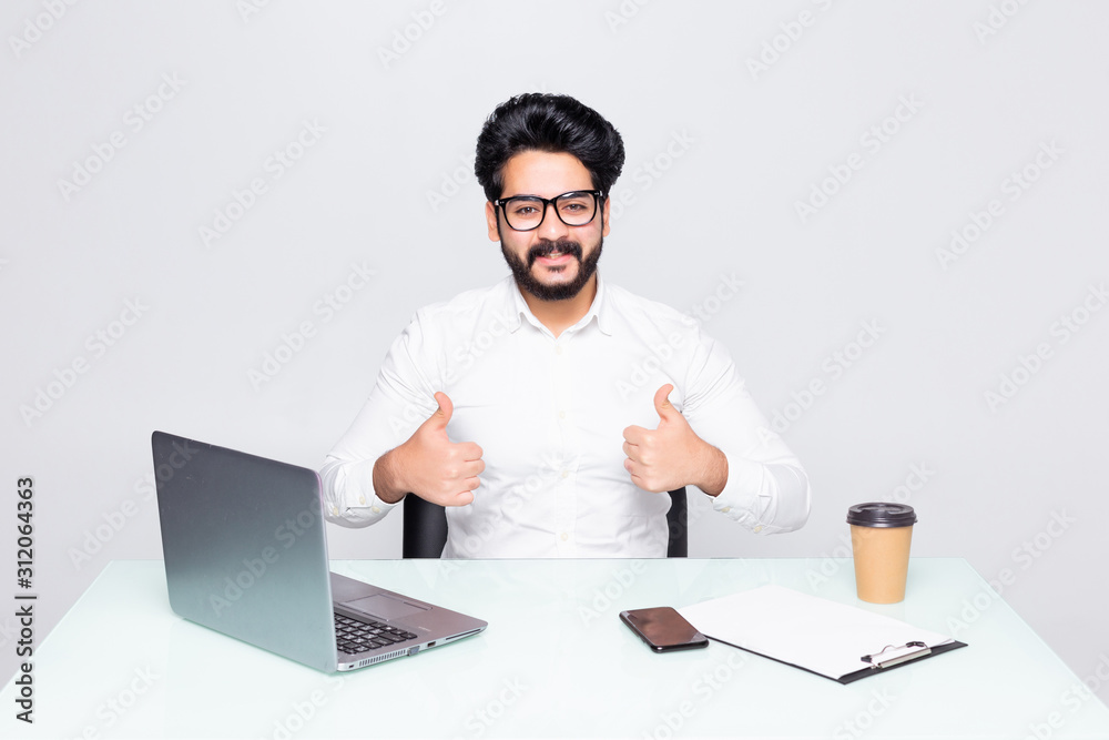Young businessman with thumbs up at office desk isolated on the white background Young businessman with thumbs up at office desk isolated on the white background