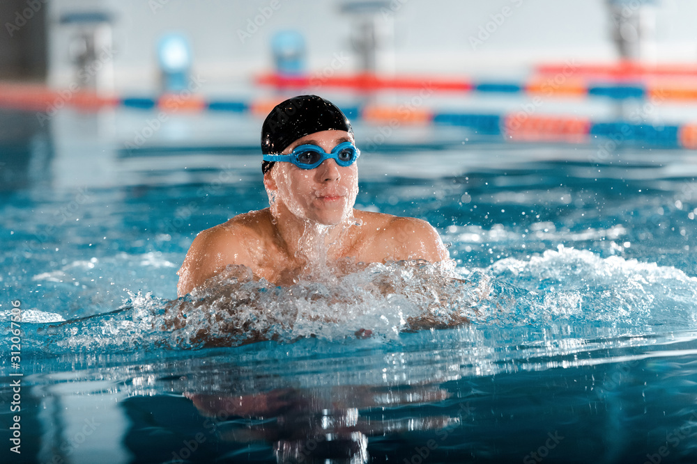 selective focus of handsome athletic man in goggles and swimming cap in swimming pool
