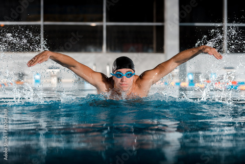 selective focus of handsome sportsman swimming butterfly stroke in swimming pool