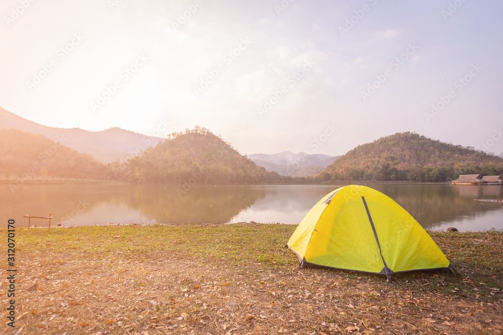 Tent Camping  beside the canal and mountains in the forest. Yellow tent on the green grass at Hoop Khao Wong Reservoir in the evening at Suphan Buri province ,Thailand.