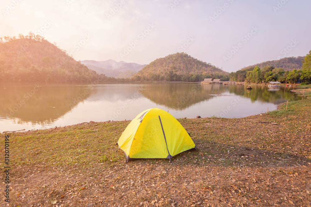 Tent Camping  beside the canal and mountains in the forest. Yellow tent on the green grass at Hoop Khao Wong Reservoir in the evening at Suphan Buri province ,Thailand.
