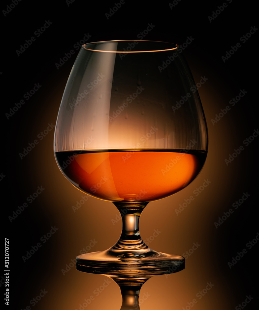 Snifter glass with cognac, brandy on a reflective surface on dark background. Snifter glass with cognac, brandy on a reflective surface on dark background.