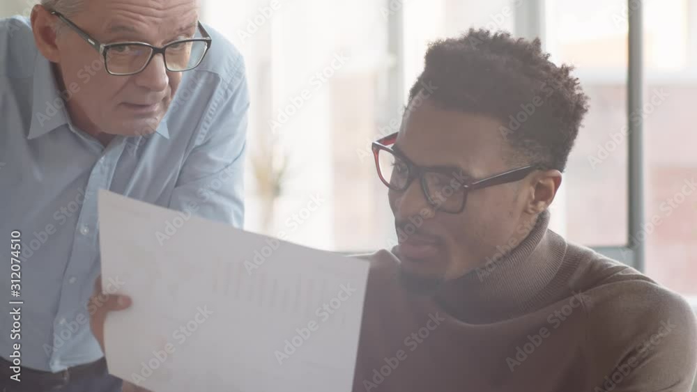 Close-up shot of multinational corporate sales team looking and pointing to performance chart and arguing during emotional business meeting in office