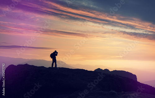 Silhouette of photographer, tourist on the edge of cliff at sunrise. Mountain valley during bright sunset. Beautiful natural landscape in the summer time. Man on top of mountain. Conceptual scene.