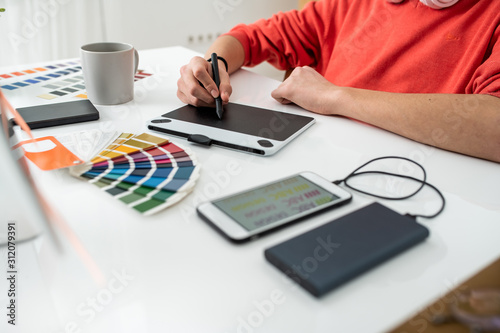 Hands of young freelance web designer holding stylus over graphics tablet screen