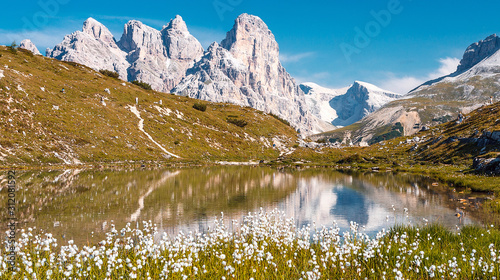 Amazing Nature Landscape. Alpine lake with crystal clear water and frash grass and flowers. Perfect Blue sky and mountains peaks. Incredible view of Dolomites Alps. Tre Cime di Lavaredo National park.