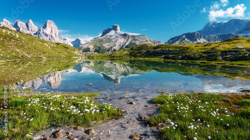 Fototapeta Naklejka Na Ścianę i Meble -  Amazing Nature Landscape. Alpine lake with crystal clear water and frash grass and flowers. Perfect Blue sky and mountains peaks. Incredible view of Dolomites Alps. Tre Cime di Lavaredo National park.