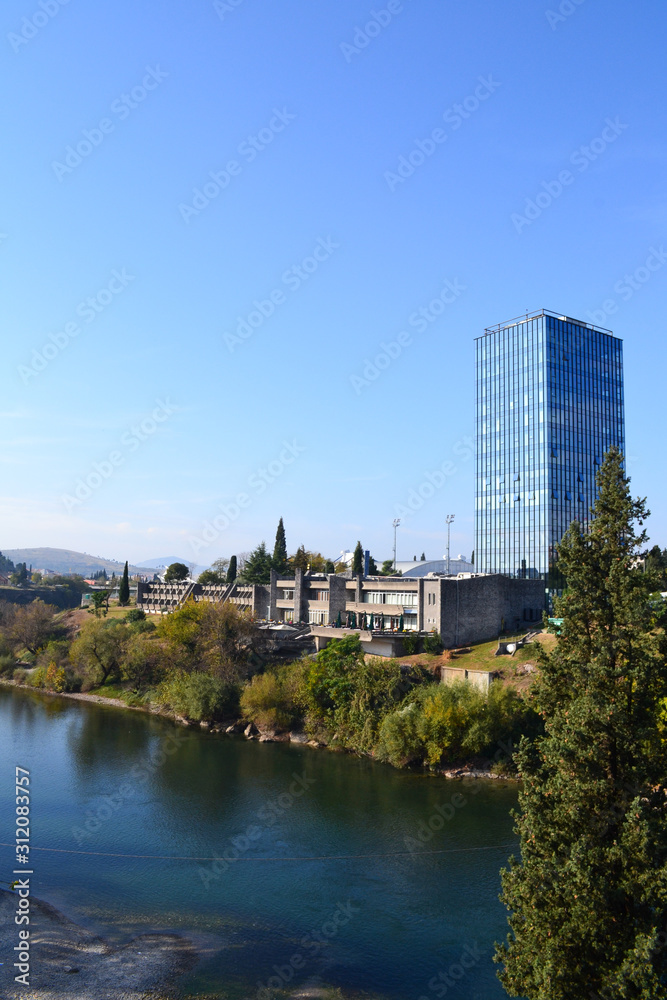 Skyscraper watching on blue clear river. Green cypress.Podgorica. Montenegro