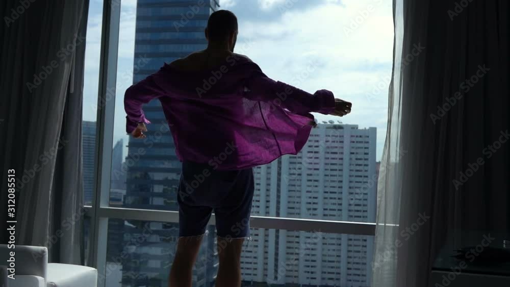 Silhouette of young man taking off shirt by window at home, super slow motion Silhouette of young man taking off shirt by window at home, super slow motion