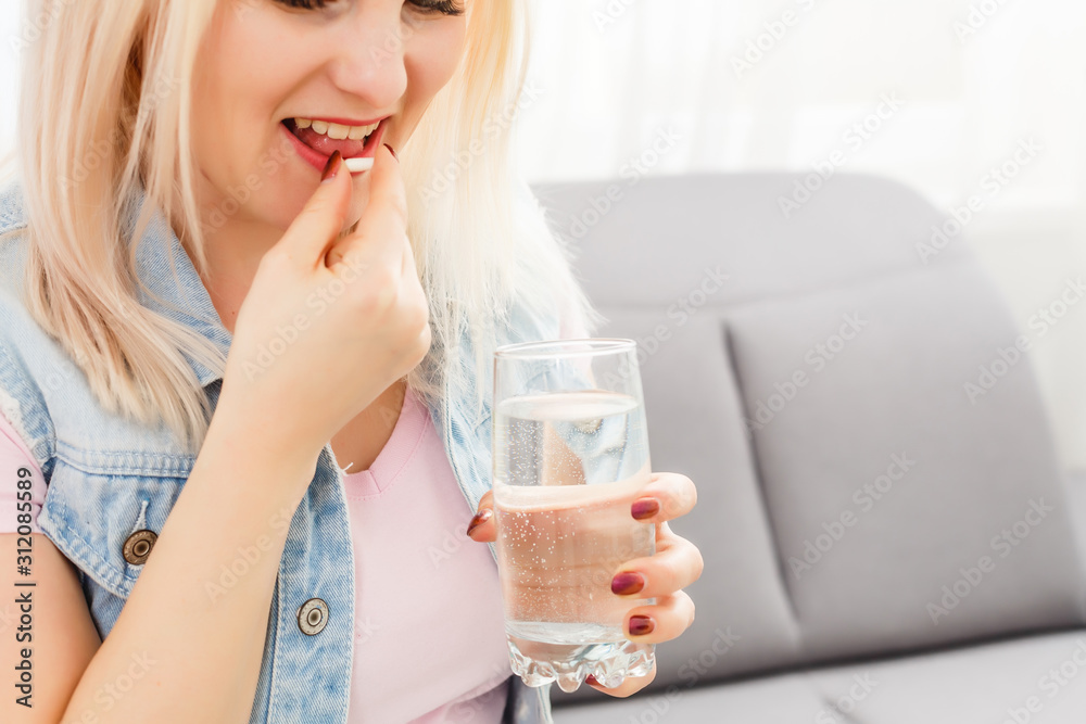 Happy young woman sitting on sofa and taking pill Happy young woman sitting on sofa and taking pill