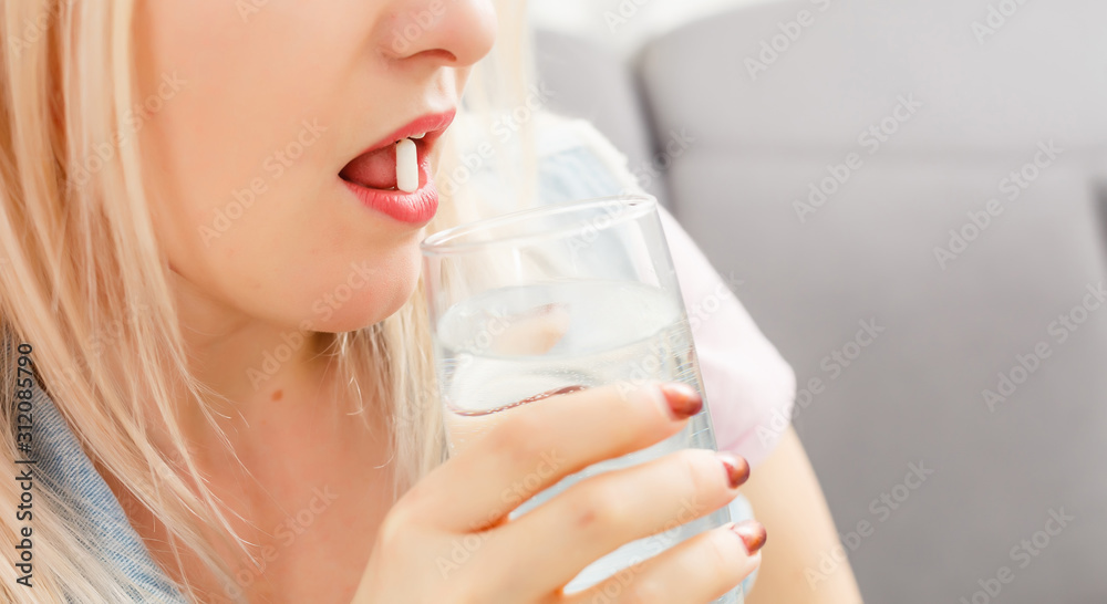 Happy young woman sitting on sofa and taking pill Happy young woman sitting on sofa and taking pill
