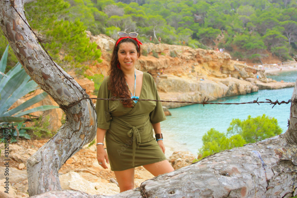caucasian girl on the cliff of cala saladeta enjoys summer vacation in the wild nature of the balearic islands