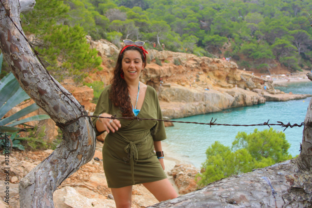 Naklejka premium caucasian girl on the cliff of cala saladeta enjoys summer vacation in the wild nature of the balearic islands