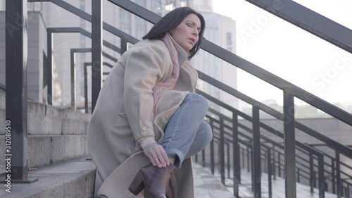 Wallpaper Mural Side view of young attractive Caucasian woman sitting on stairs with ankle pain. Young brunette businesswoman suffering because of fast pace of life. Hardworking, overworking, healthcare. Torontodigital.ca